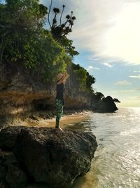 Man standing on rock by sea against sky