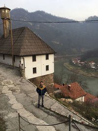 Man standing on house by buildings against mountain