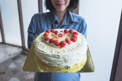 Midsection of young woman holding valentine cake at home