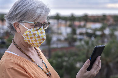 Senior woman wearing mask while using mobile phone outdoors