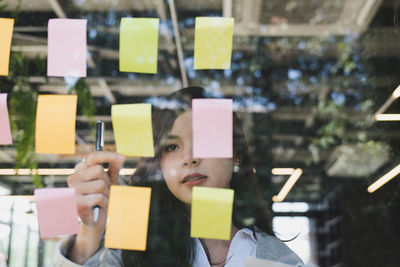 Young woman holding yellow adhesive note on glass