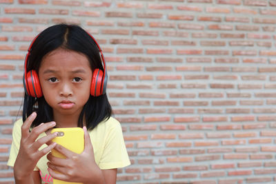 Portrait of girl holding smart phone against wall