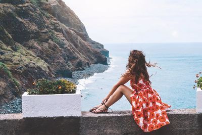 Woman sitting on wall over sea against sky