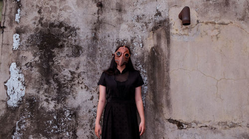 Portrait of young woman with halloween mask standing against wall