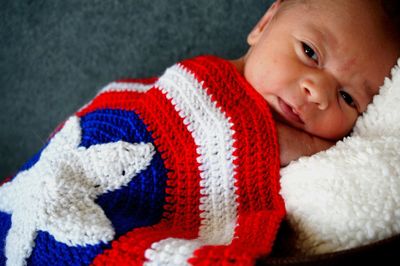 Close-up portrait of baby boy covered with knitted blanket lying on bed