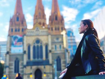 Young woman looking away by cathedral in city