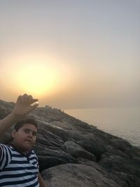 Woman on rock at beach against sky during sunset