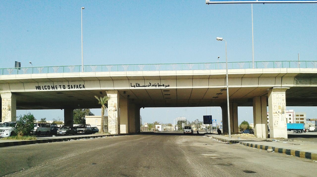 transportation, built structure, architecture, road, text, clear sky, connection, bridge - man made structure, road marking, western script, street, the way forward, communication, car, building exterior, sign, information sign, city, road sign, guidance