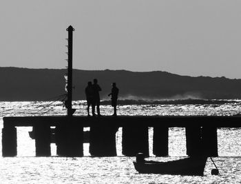 Silhouette people standing by sea against clear sky