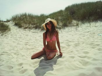 Woman wearing bikini sitting at sandy beach