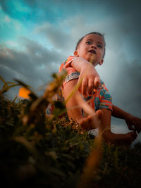 Low angle view of cute baby girl on field against sky