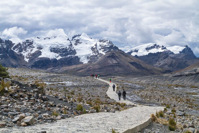 People walking on footpath against snowy mountains