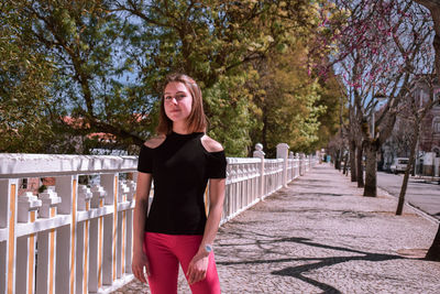 Portrait of woman standing by railing against trees