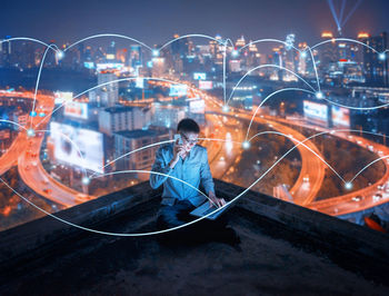 Digital composite image on man talking on mobile phone and using laptop with connecting dots in city