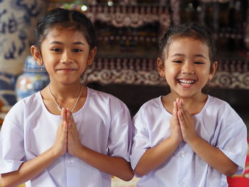 Portrait of smiling sisters in praying position standing in temple