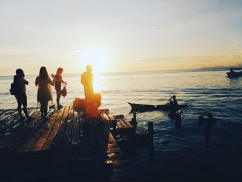 People standing by sea on pier during sunset