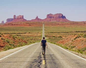 Full length rear view of man walking on road against clear sky