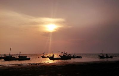 Silhouette boats moored in sea against sky during sunset