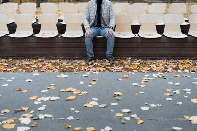 Low section of man sitting on chair by autumn leaves