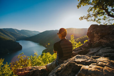 Rear view of woman sitting on rock against mountain