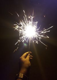 Cropped hand holding sparkler at night