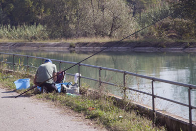 Man with fishing equipment kneeling on bridge over river