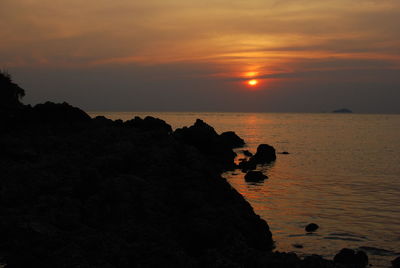 Silhouette rocks on shore against sky during sunset