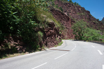 Empty road amidst trees against mountains