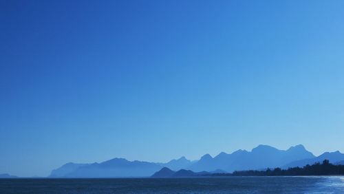 Scenic view of sea and mountains against clear blue sky