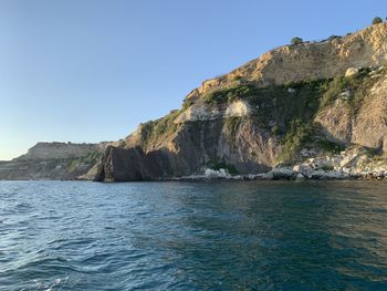 Rock formations by sea against clear blue sky