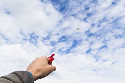 Low angle view of hand holding flying kite against sky
