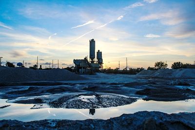 Factory on snow covered landscape against sky during sunset