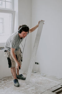 Young caucasian male plasterer listens to music through headphones and cleans the putty trowel