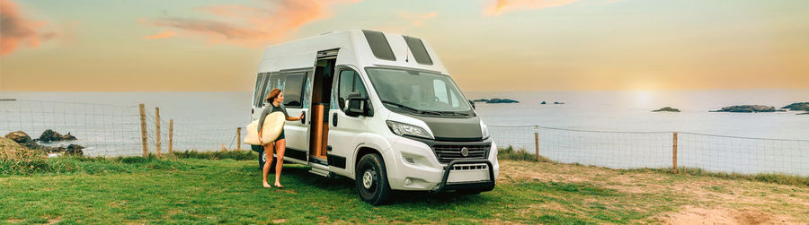 Woman with wetsuit and surfboard closing the door of her camper van to go surfing