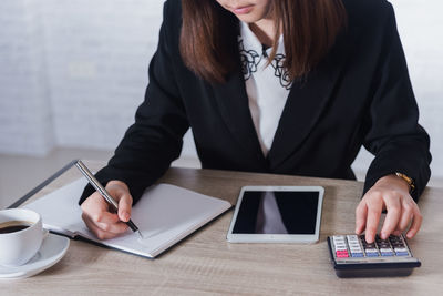 Midsection of businesswoman doing calculation in office