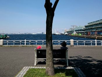 Rear view of man sitting at sea against clear sky