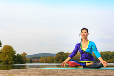 Woman practicing yoga on pier against sky