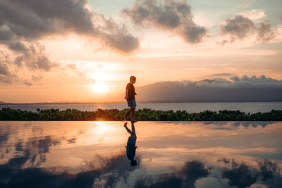 Full length of man standing on shore against sky during sunset