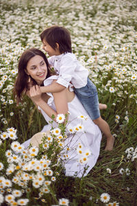 Woman in a white dress with her son, fun in a chamomile field at sunset in summer