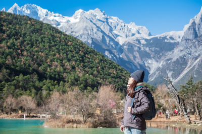 Side view of woman wearing backpack while standing against mountains during winter