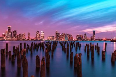 Wooden posts in sea against illuminated skyline