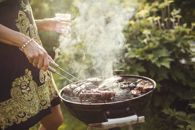 Midsection of woman grilling meat on barbecue in back yard