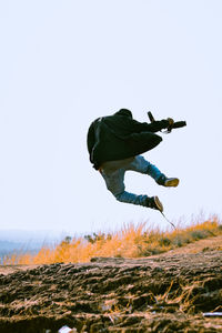 Low angle view of man jumping on field against clear sky