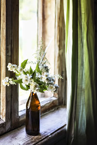 A bottle with blooming jasmine branches by the window in a rustic house.
