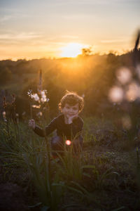 Boy on field against sky during sunset