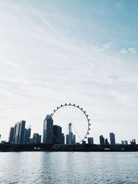 Low angle view of ferris wheel and buildings by river against sky