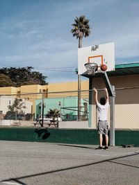 Full length of man playing basketball in court against sky