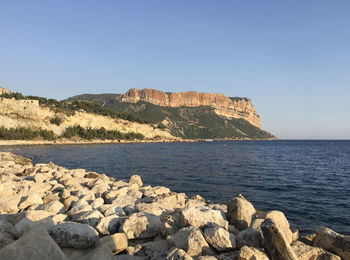 Scenic view of rocks by sea against clear blue sky