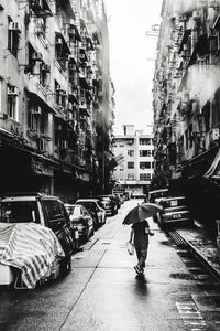 Rear view of people walking on street amidst buildings in rainy season