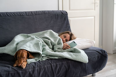 Woman relaxing on sofa with dog while using mobile phone
